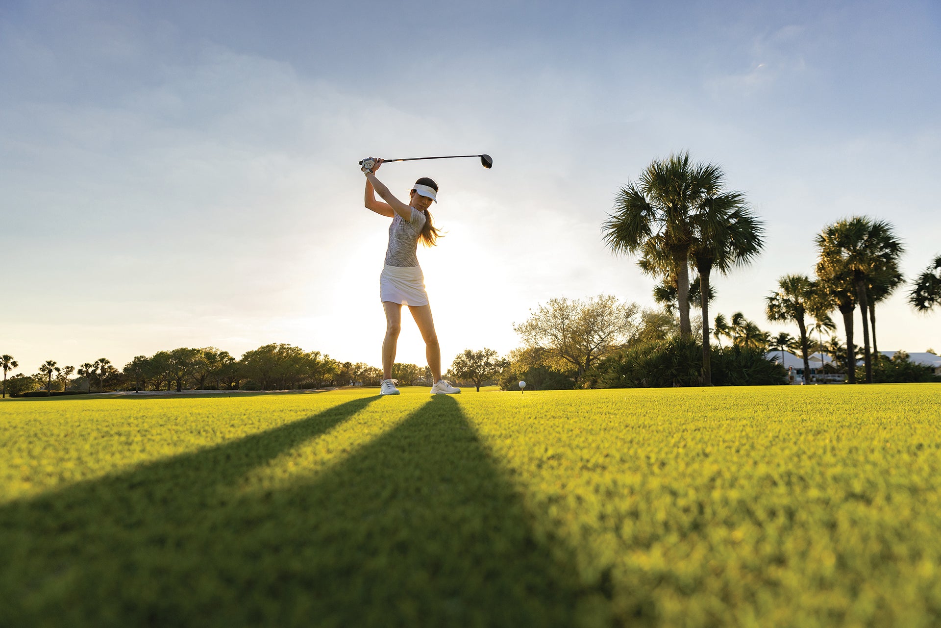 A woman in her backswing on the golf course with the sun shining behind her