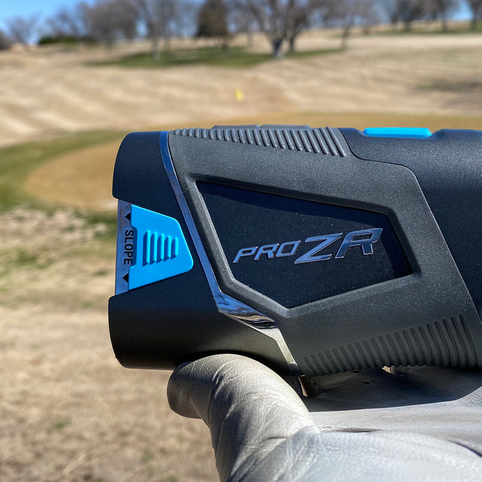 The Shot Scope PRO ZR golf rangefinder in a golf-gloved hand held up against a golf course in the background