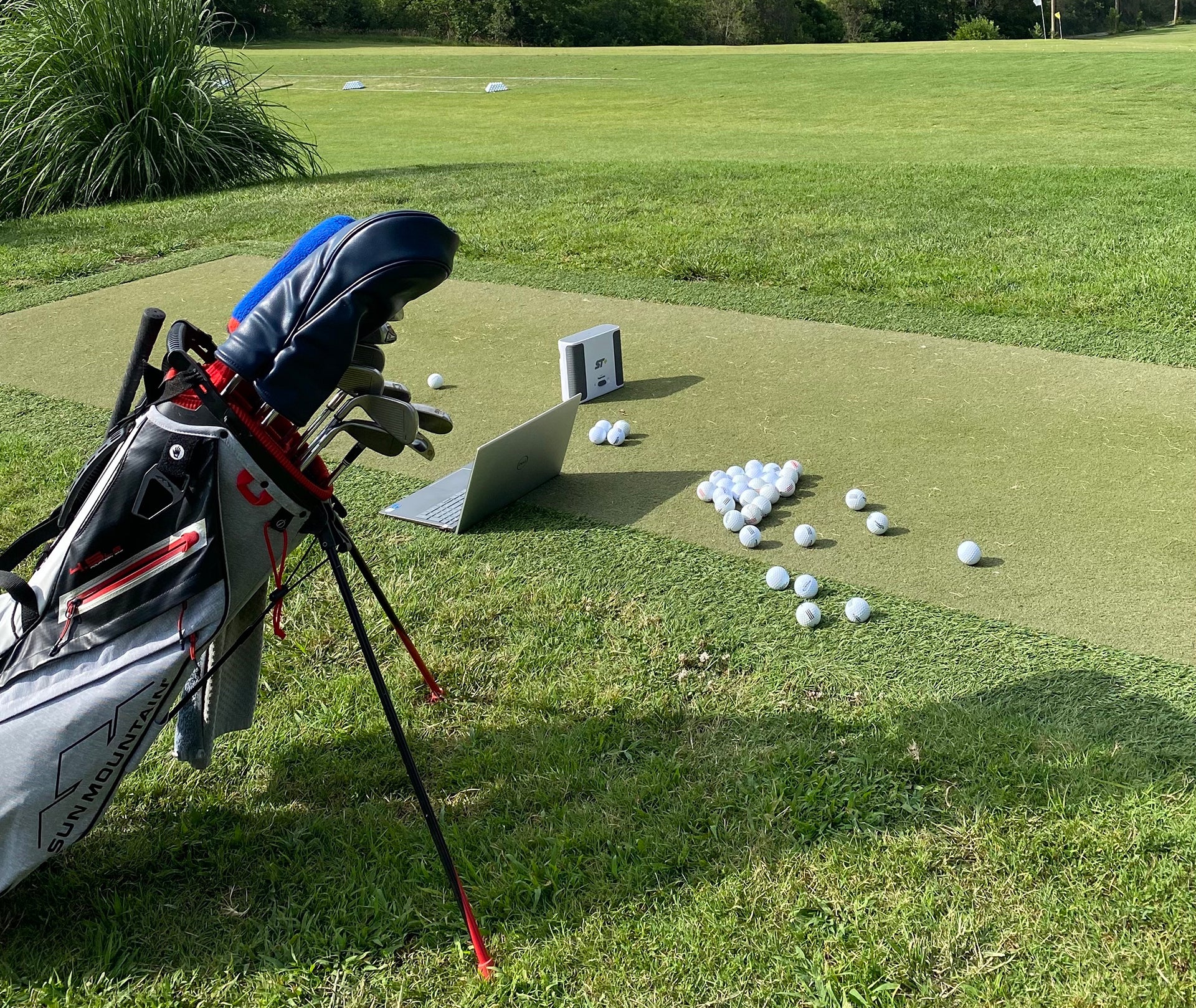Golf reviewer Marc's golf bag, golf balls, laptop, and SkyTrak+ sitting at the golf range 