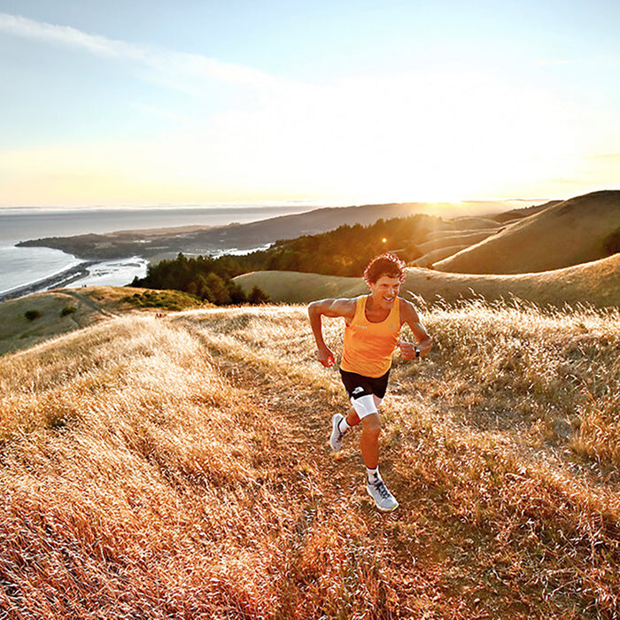 Marathoner Dean Karnazes running up a hill of golden grass with the coast and ocean below and behind him