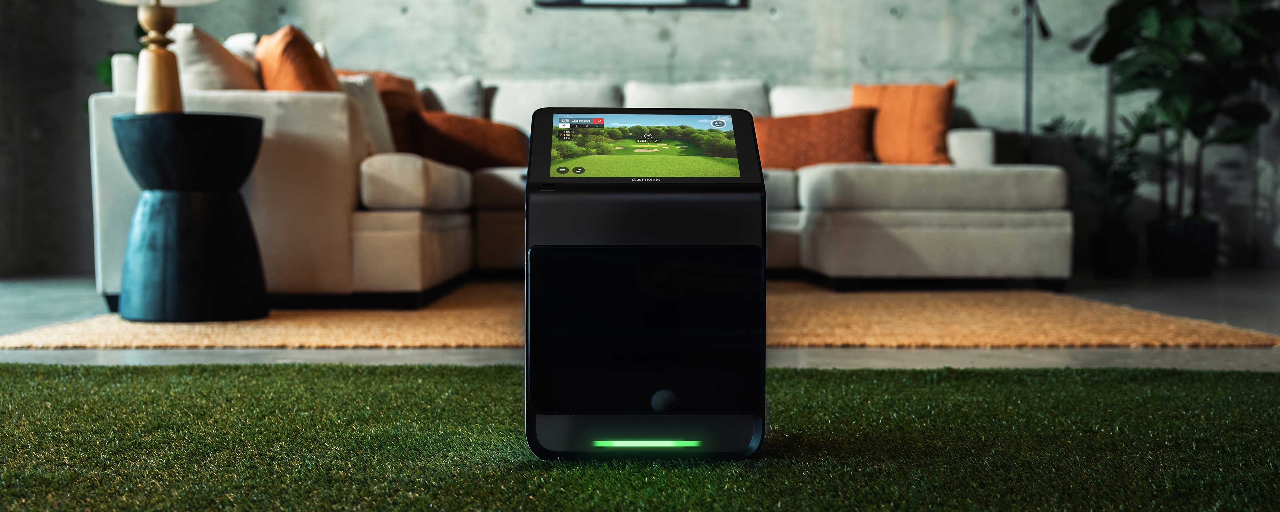 The Garmin Approach R50 launch monitor with built-in golf simulator on a golf hitting mat in a modern living space with a sectional couch behind it