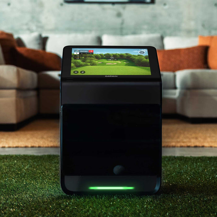 The Garmin Approach R50 launch monitor with built-in golf simulator on a golf hitting mat in a modern living space with a sectional couch behind it