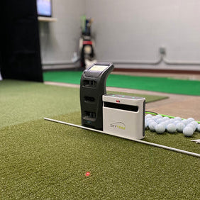 The SkyTrak+ launch monitor next to the Foresight Sports GC3 next to many golf balls and golf tees on a golf mat in an indoor simulator