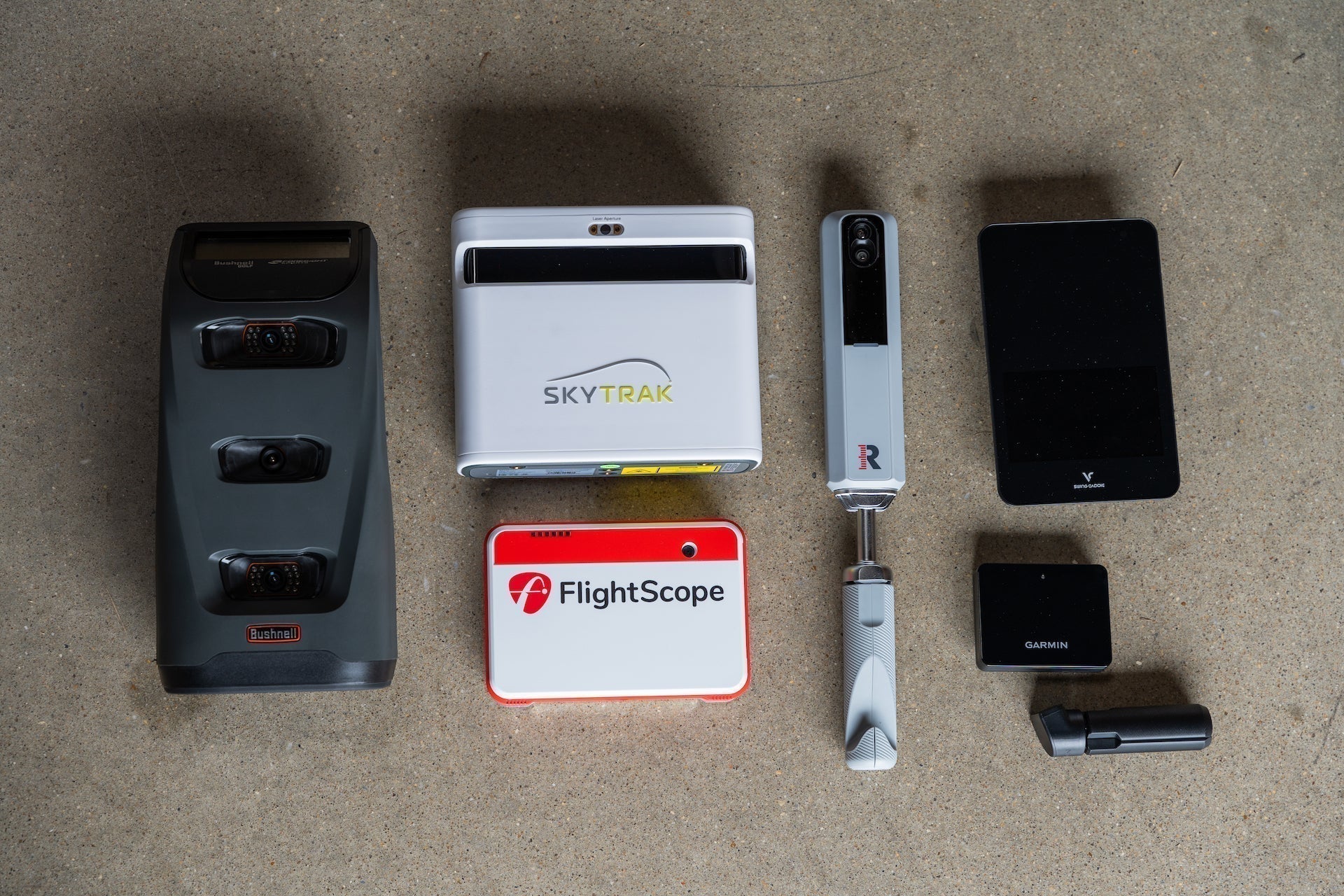 Several golf launch monitors from the PlayBetter collection—including Launch Pro, SkyTrak+, MLM2PRO, Garmin R10, Swing Caddie SC4, and Mevo+—laying together on the floor