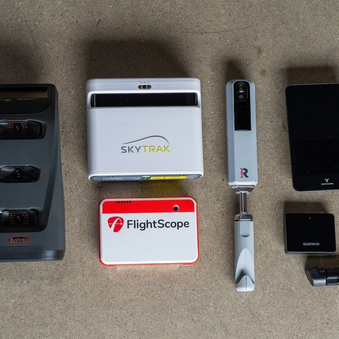 Several golf launch monitors from the PlayBetter collection—including Launch Pro, SkyTrak+, MLM2PRO, Garmin R10, Swing Caddie SC4, and Mevo+—laying together on the floor
