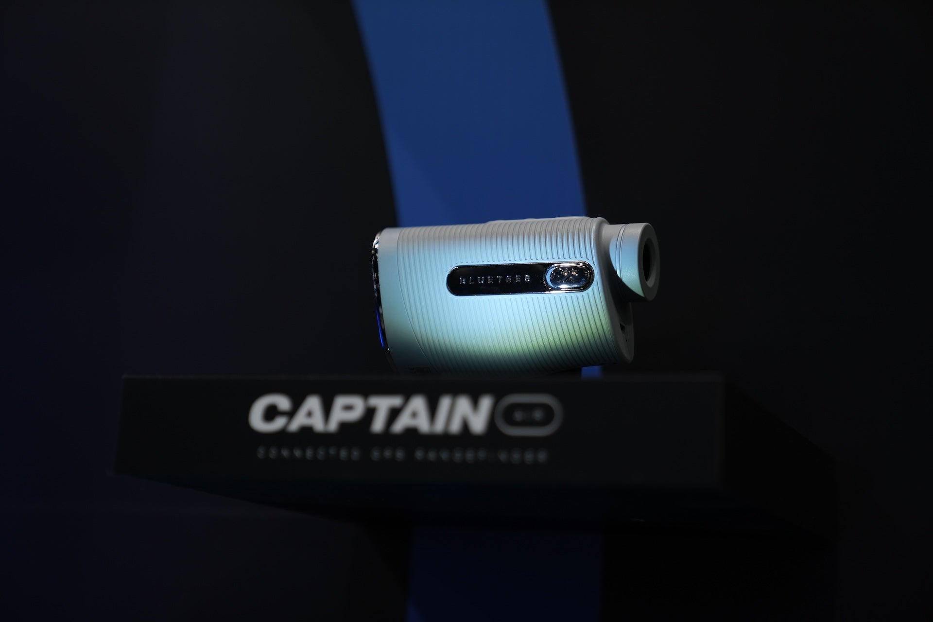 The Blue Tees Captain Air laser rangefinder on display in a spotlight with the CAPTAIN name below it