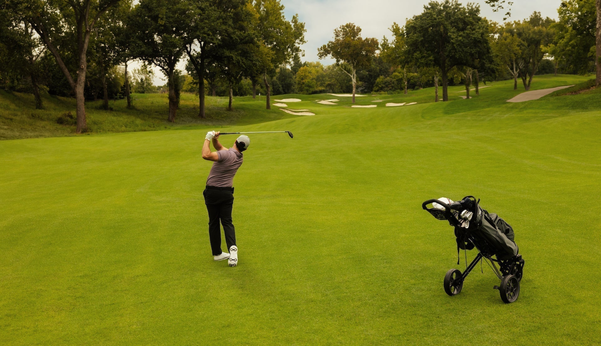 Golfer post swing hitting on a golf course with a golf bag push card