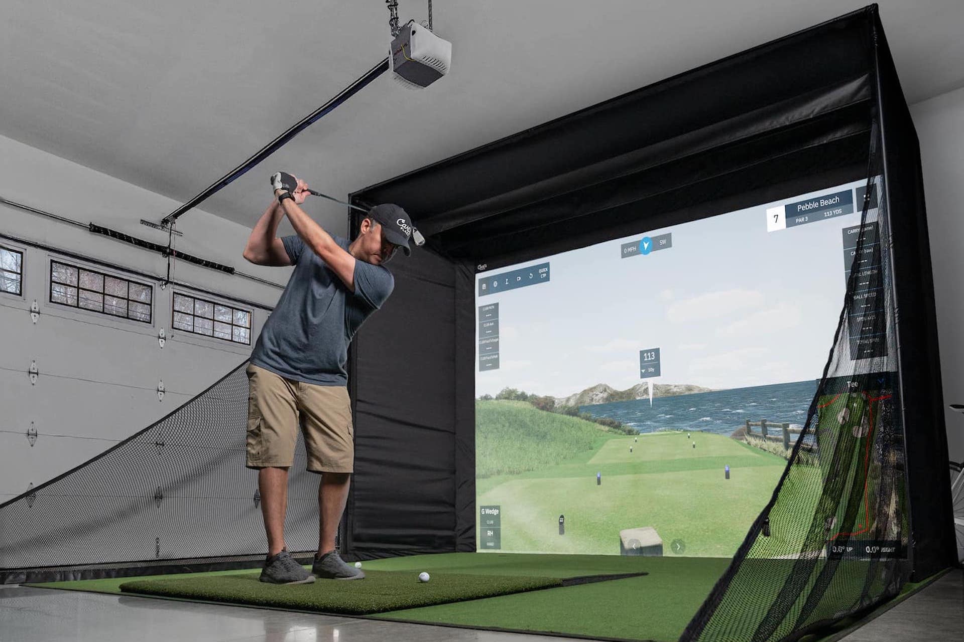 A golfer swinging in a Carl's Place golf simulator setup in a garage