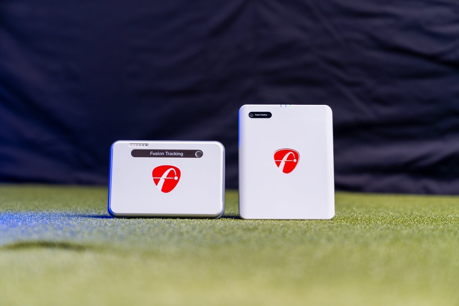 The FlightScope Mevo Plus next to the Mevo Gen2 on a golf hitting mat in a golf simulator