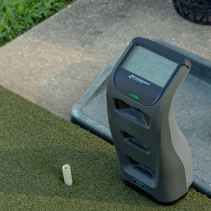 The Foresight GC3 launch monitor with data on the display sitting on a golf hitting mat next to the tee and a ball tray at a hitting range