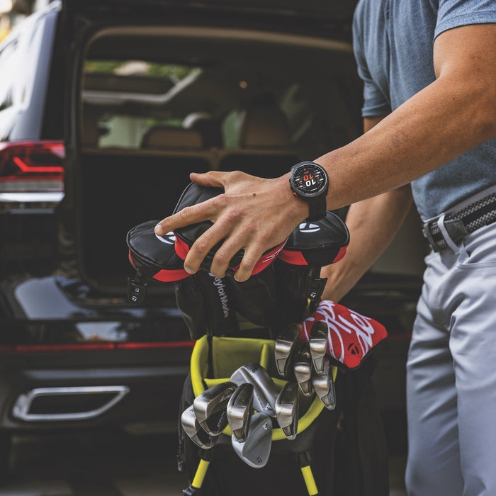 A golfer wearing a Garmin Approach S70 golf watch as he pulls his golf bag out of the rear of his SUV