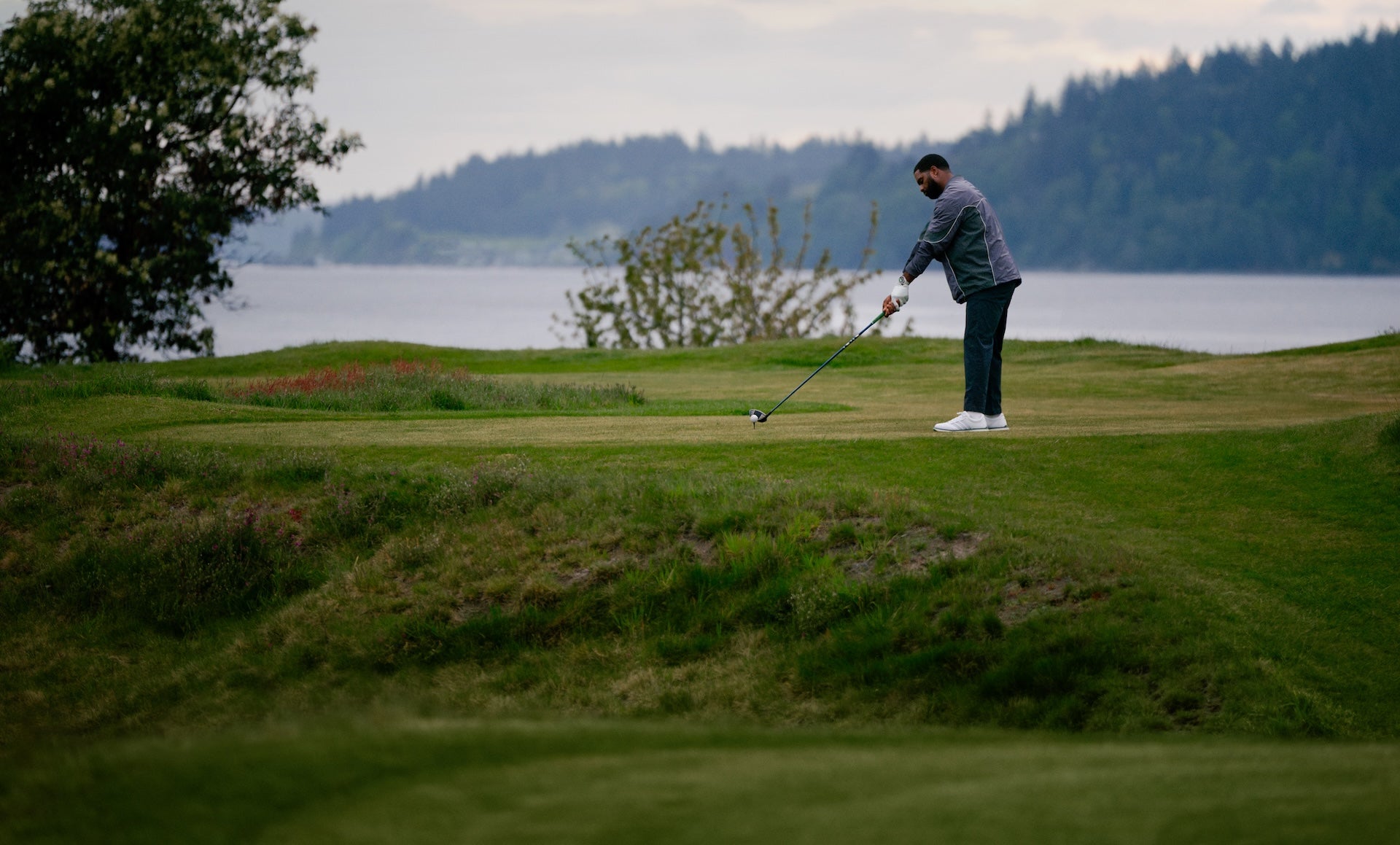 A golfer getting ready to take a shot on a golf course by a body of water wearing a Garmin Approach S72 golf watch