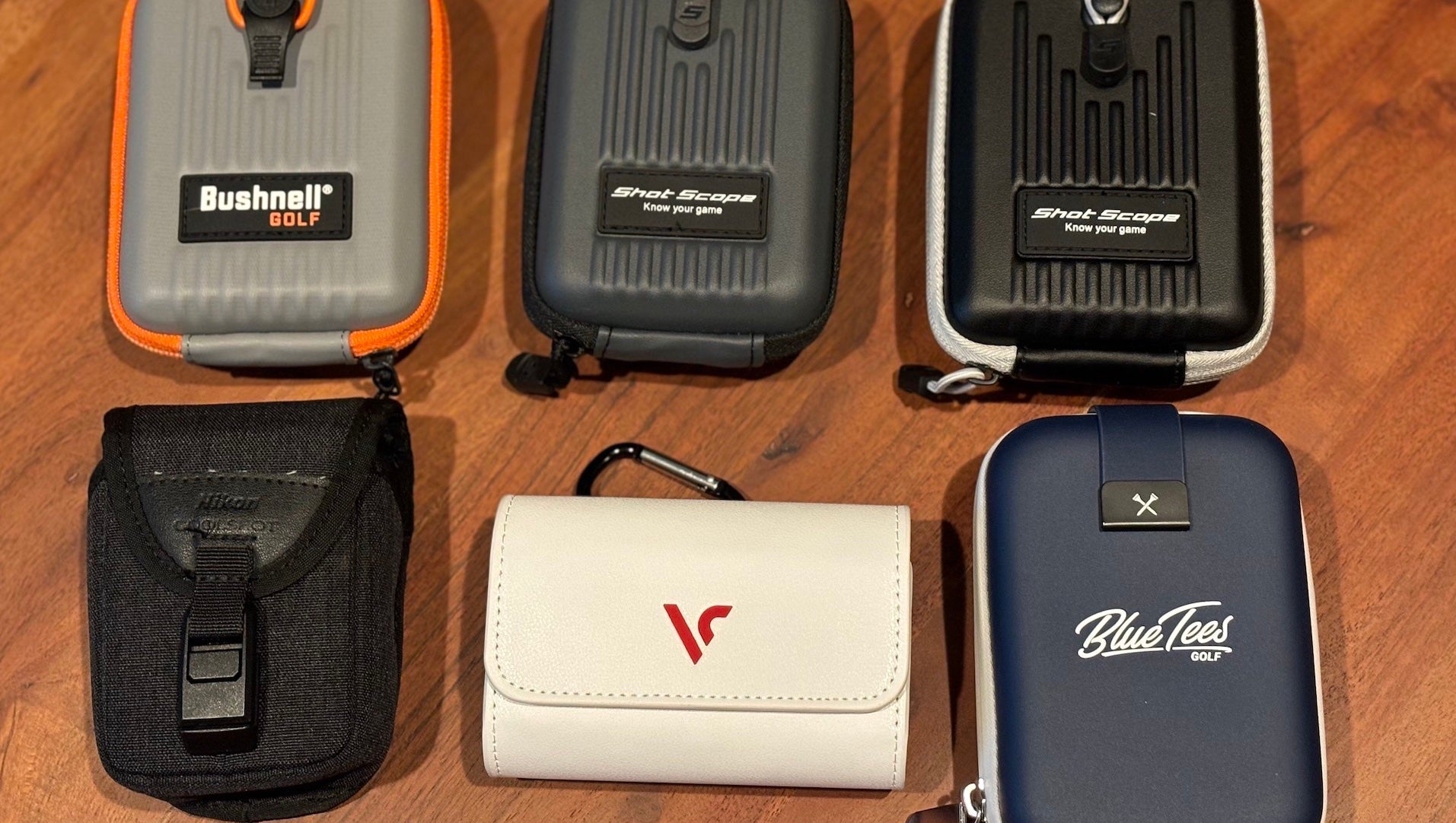 Six golf rangefinder cases with various top golf brand names on them on a woodgrain surface