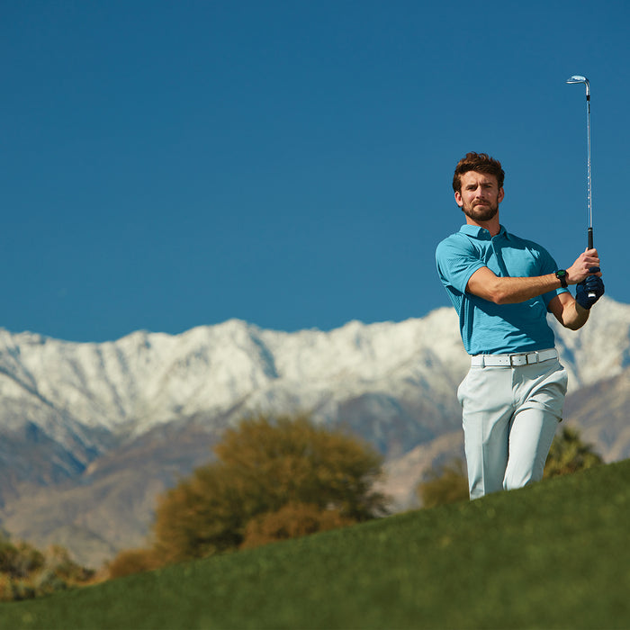 A golfer with a club post-swing on a golf course with a mountain range behind him