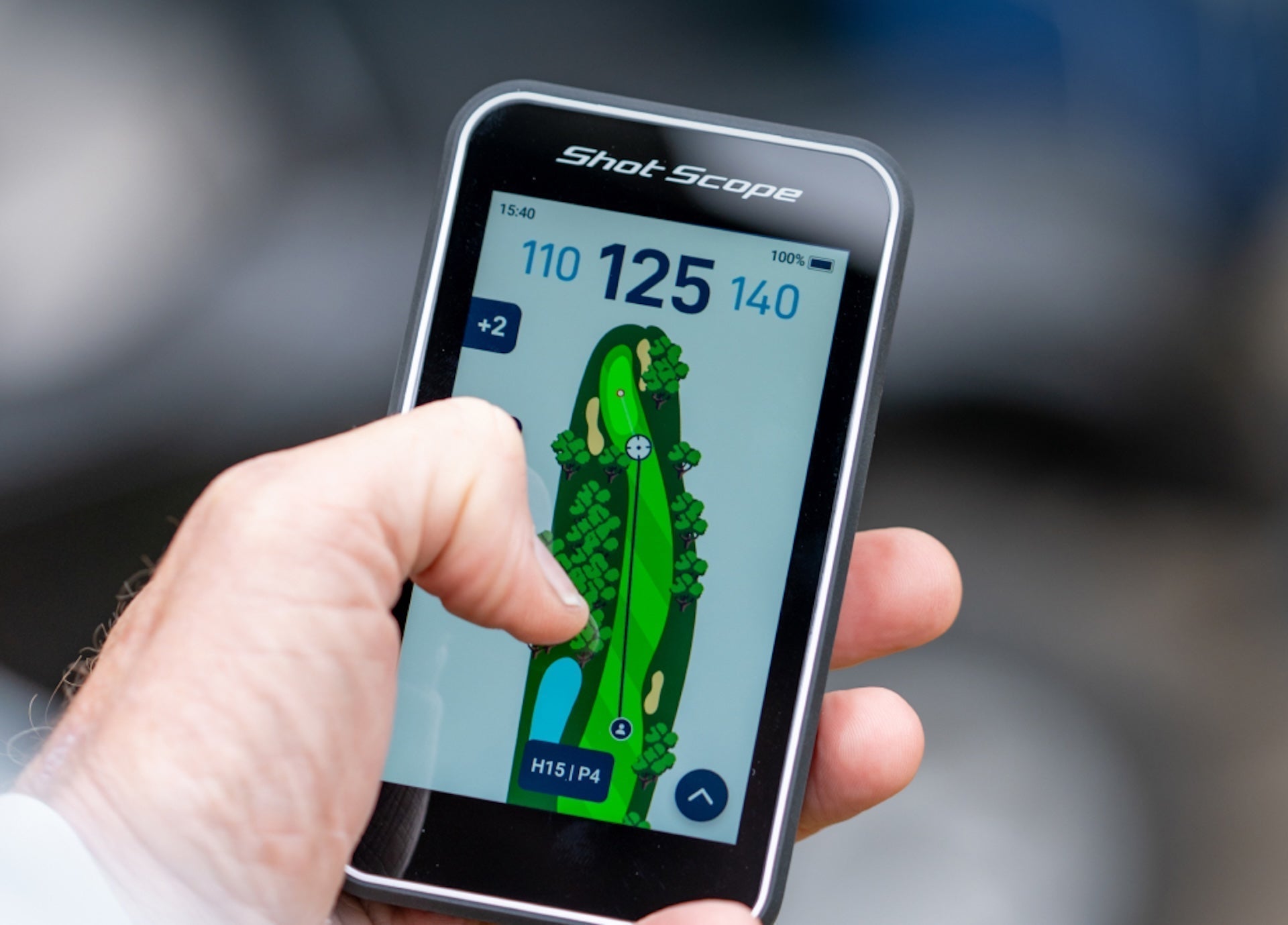 The Shot Scope H50 golf GPS handheld in a hand with golf hole graphic, features, and yardages on the display