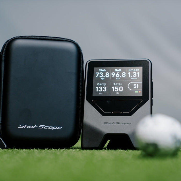 The Shot Scope LM1 on a golf hitting mat next to its carrying case and some golf balls