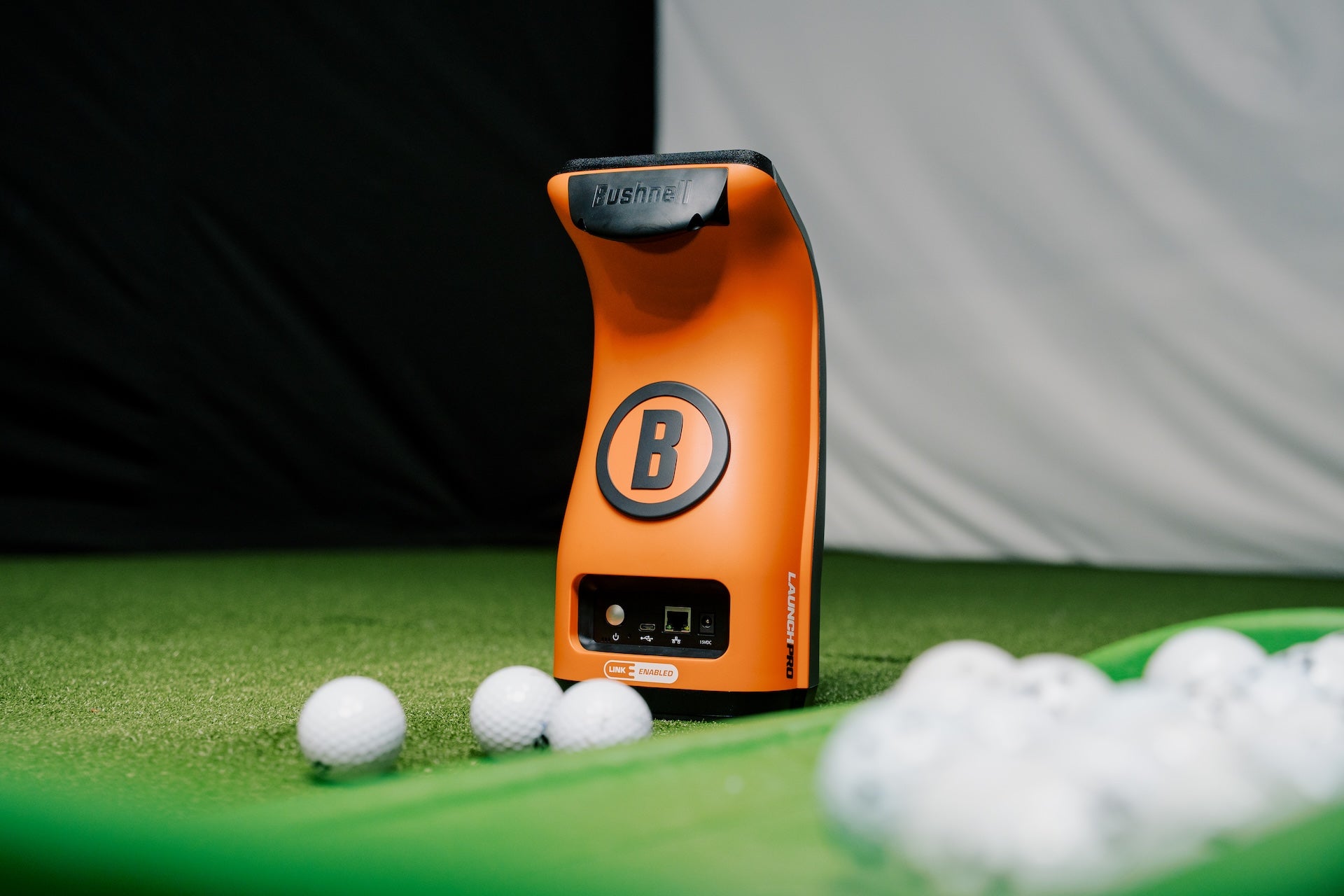 The orange and black back of the Bushnell Launch Pro launch monitor with golf balls in the PlayBetter simulator