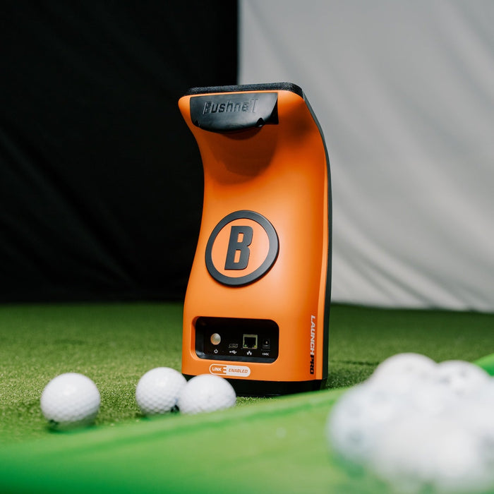 The orange and black back of the Bushnell Launch Pro launch monitor with golf balls in the PlayBetter simulator