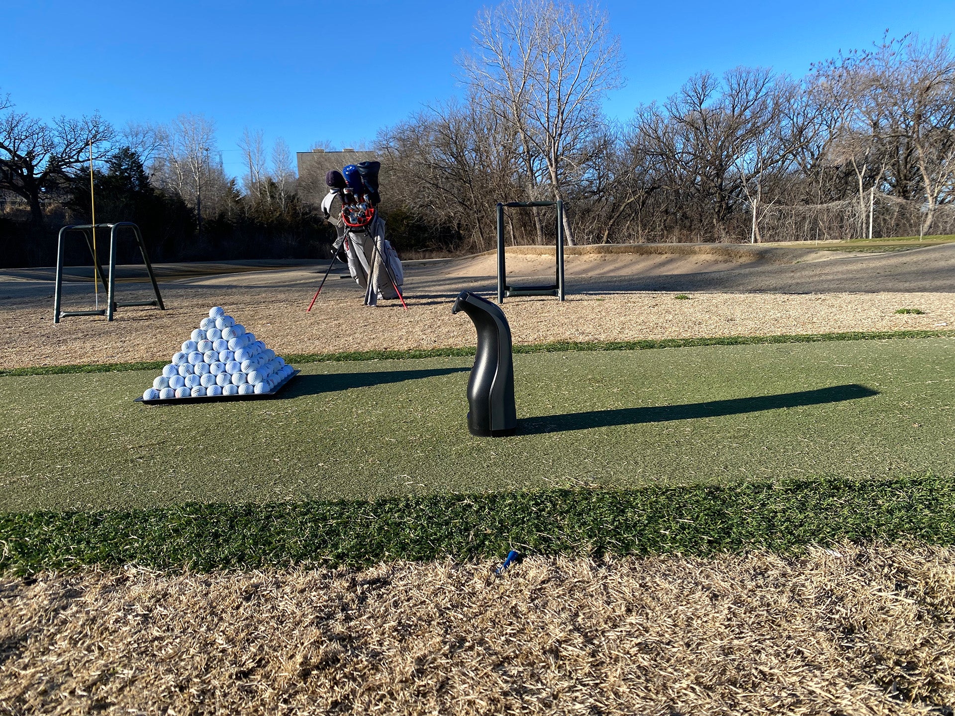 The Bushnell Launch Pro set up on the range next to a pyramid of golf balls and a golf bag in the background