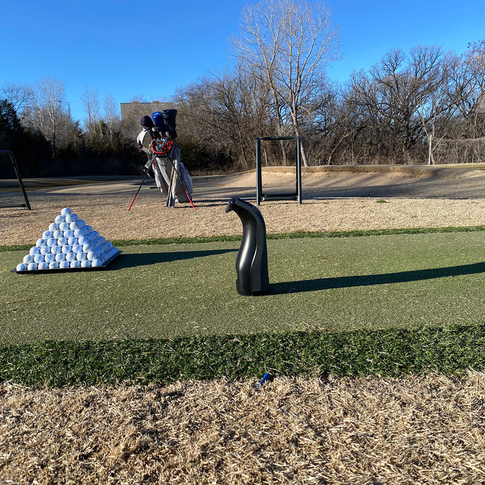 The Bushnell Launch Pro set up on the range next to a pyramid of golf balls and a golf bag in the background