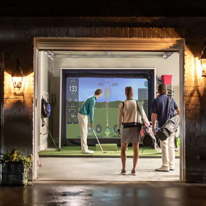 View from outside a double garage with two men watching another golfer hit into an impact screen in a garage golf simulator