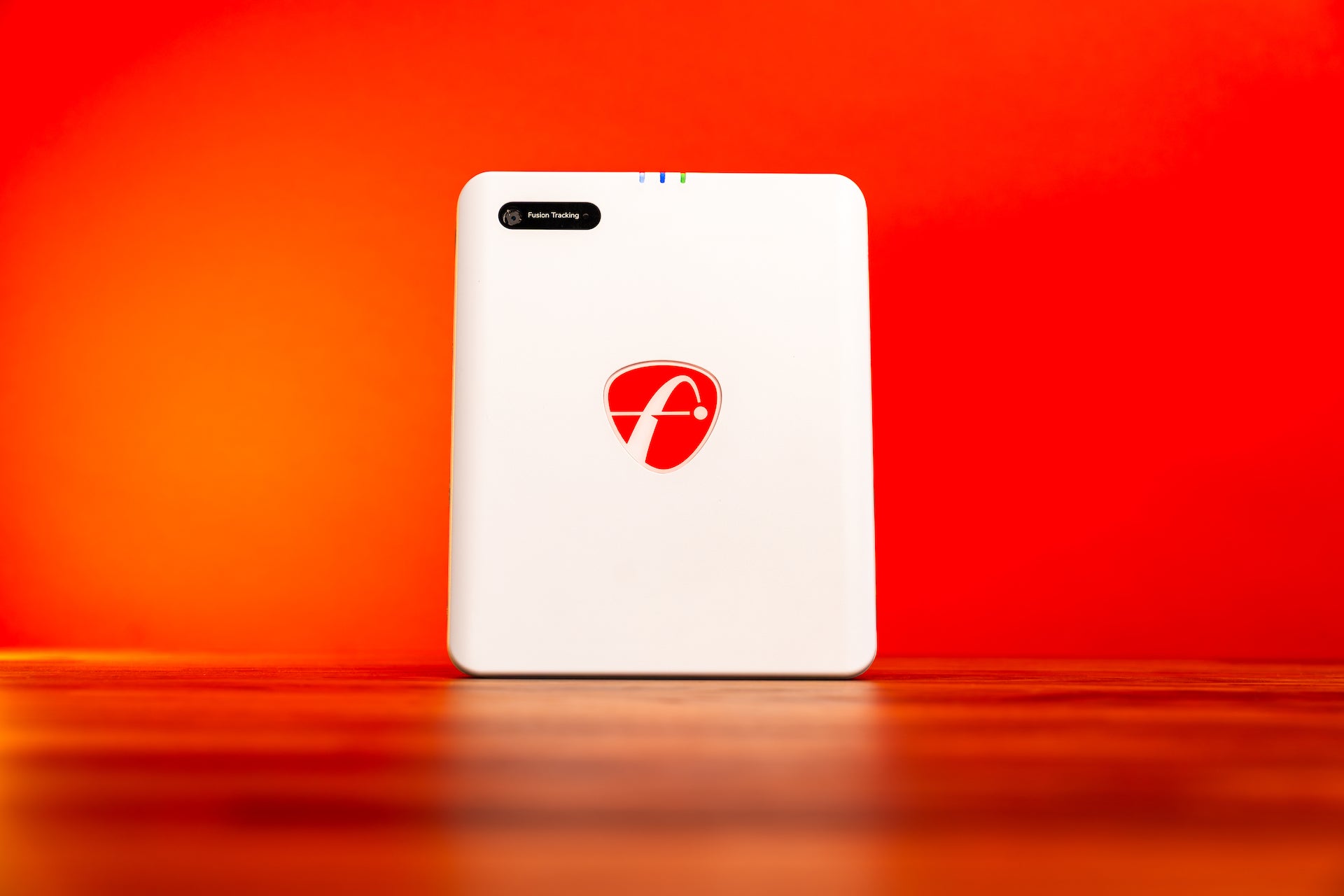 The FlightScope Mevo Gen2 sitting in front of a bright red background on a shiny woodgrain surface