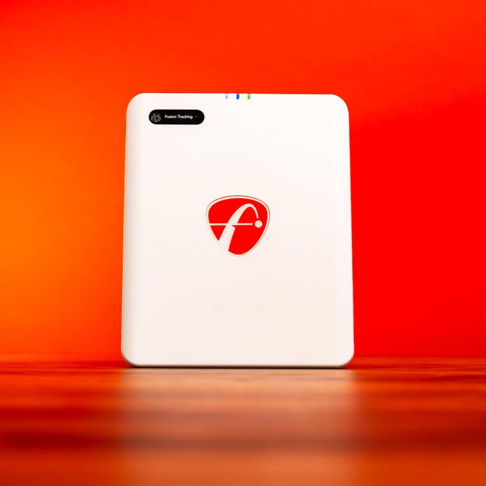 The FlightScope Mevo Gen2 sitting in front of a bright red background on a shiny woodgrain surface