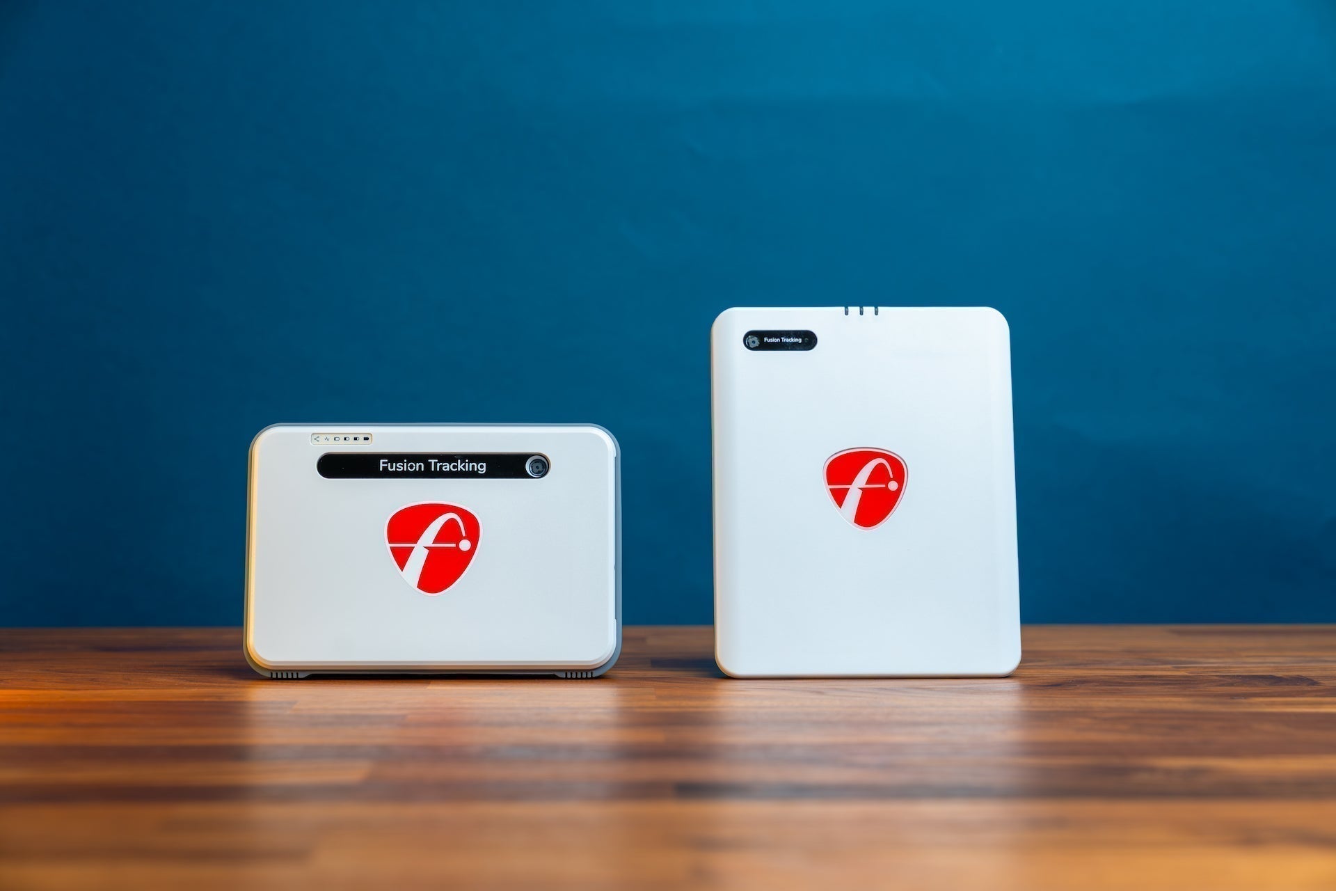 The FlightScope Mevo+ next to the new Mevo Gen2 golf launch monitor in front of a blue wall on a woodgrain surface