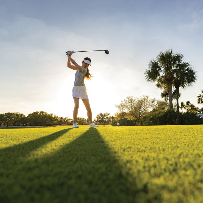 A woman in her backswing on the golf course with the sun shining behind her