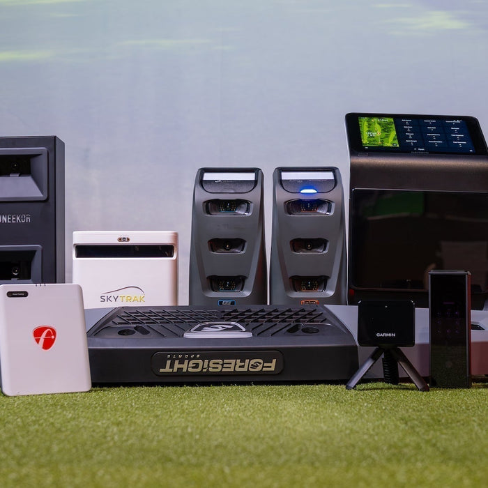 A group of golf launch monitors offered by PlayBetter on a golf hitting mat in front of a golf impact screen