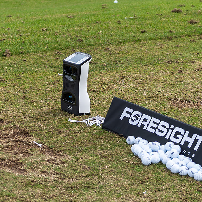 The Foresight Sports QuadMAX on the driving range next to a Foresight sign and a bunch of golf balls