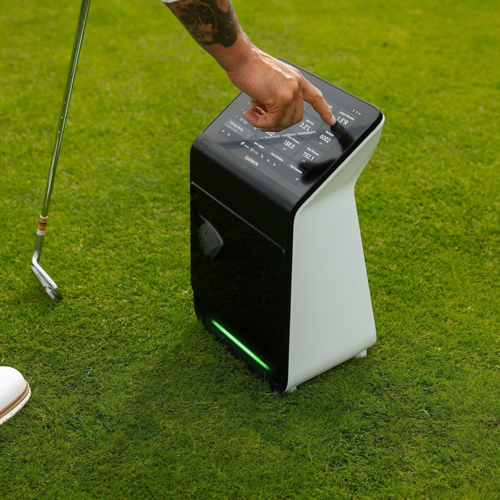 A golfer's hand touching the display of the Garmin Approach R50 at the golf hitting range