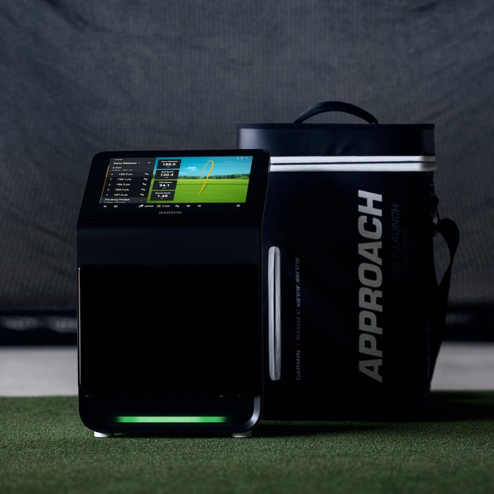 The Garmin Approach R50 next to its carrying case on a golf hitting mat in front of a golf practice net