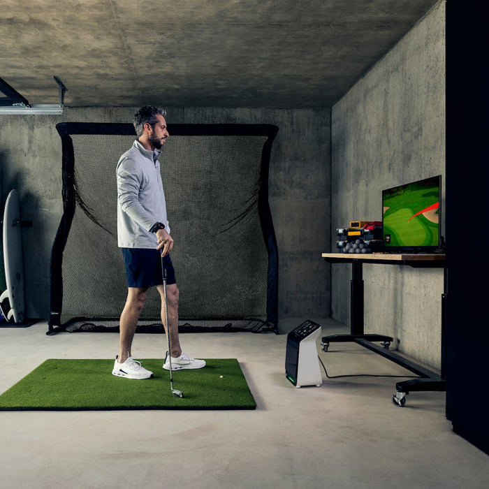 Golfer in a garage golf simulator with the Garmin Approach R50, golf hitting mat, and a golf hitting net