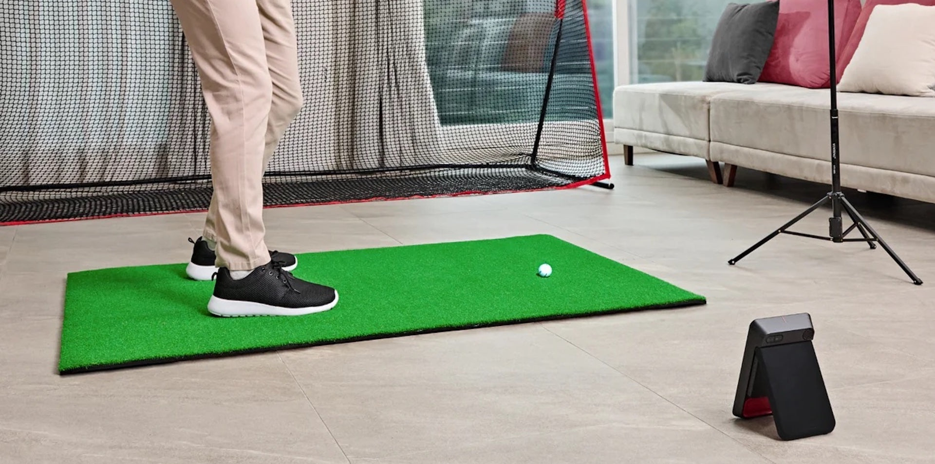 The lower half of a golfer getting ready to swing in a home golf setup in a living room with Swing Caddie SC4 Pro, golf hitting mat and golf net