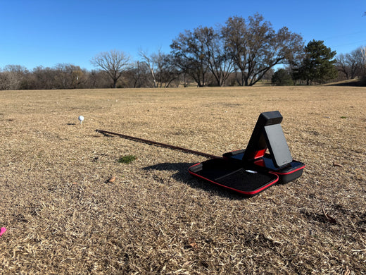 The Swing Caddie SC4 Pro at the golf range sitting on top of SC4 carrying case in front of alignment stick and golf ball