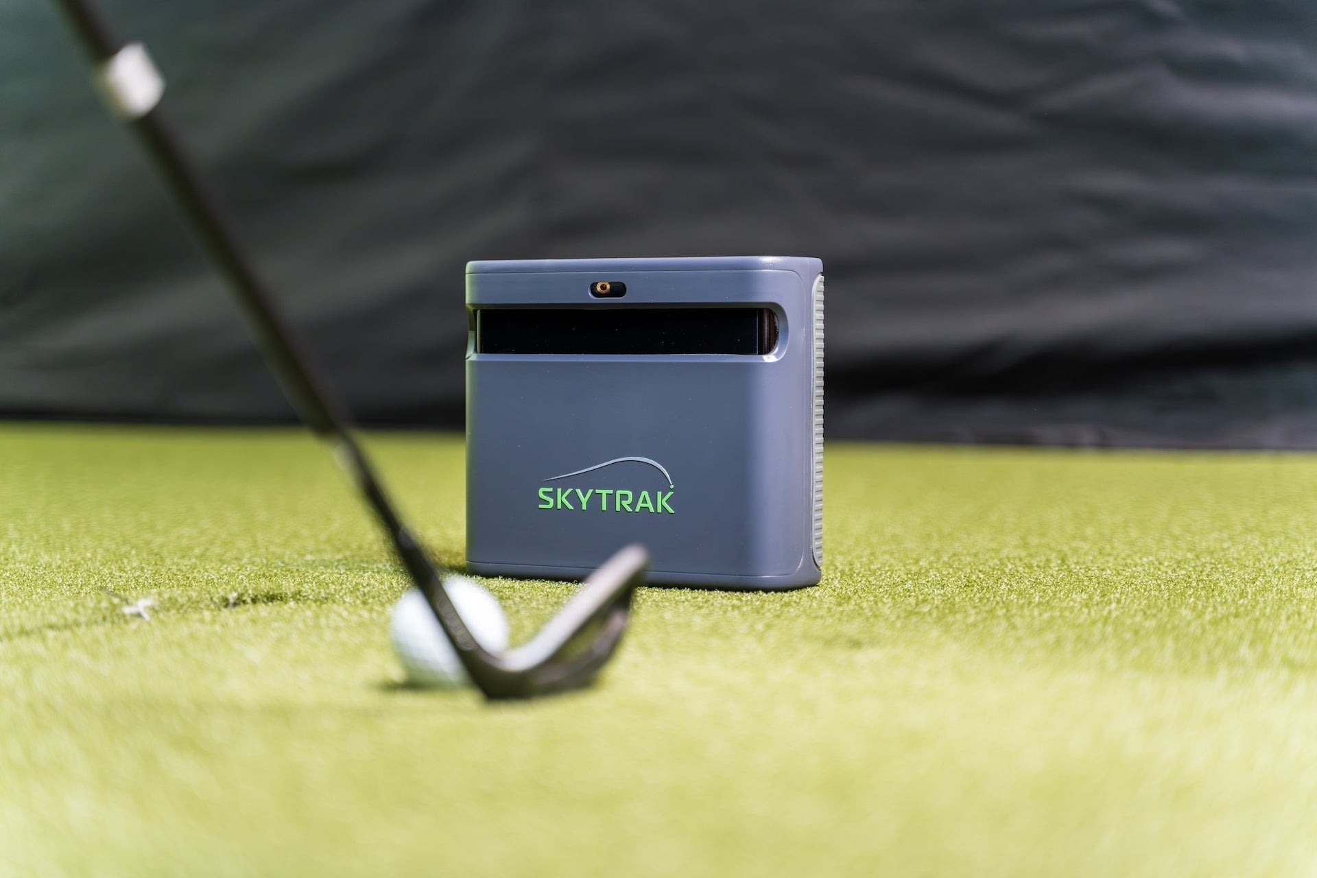 The SkyTrak ST MAX on a golf hitting mat in a simulator with a golf ball and club in front of it