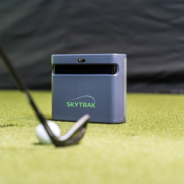 The SkyTrak ST MAX on a golf hitting mat in a simulator with a golf ball and club in front of it