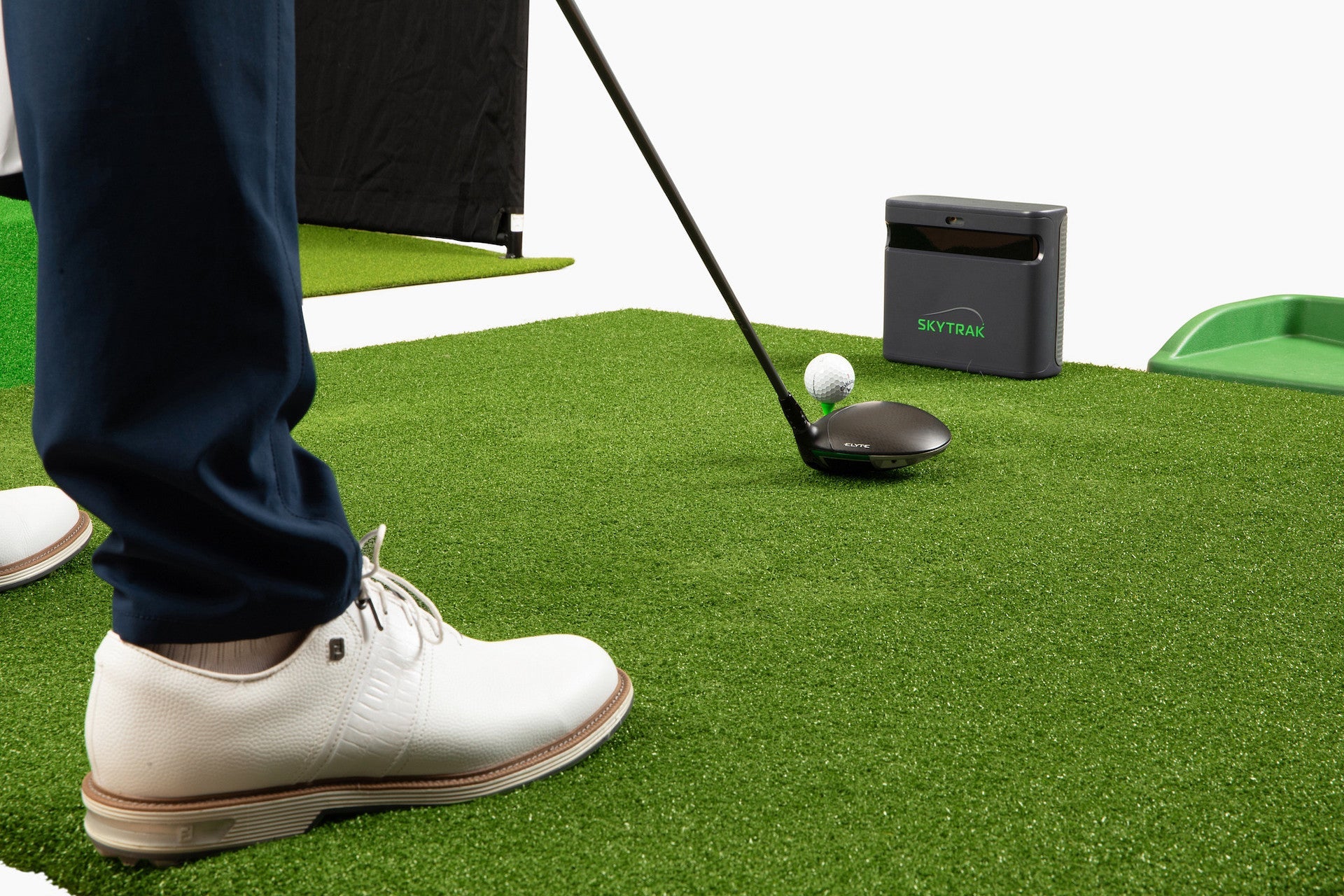 SkyTrak ST MAX on a golf mat in front of a golfer's fee and driver and golf ball