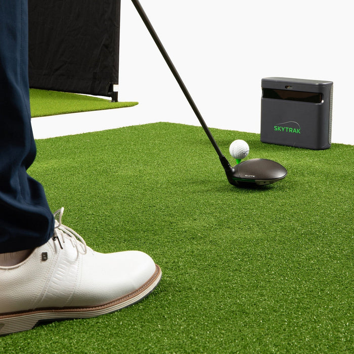 SkyTrak ST MAX on a golf mat in front of a golfer's fee and driver and golf ball