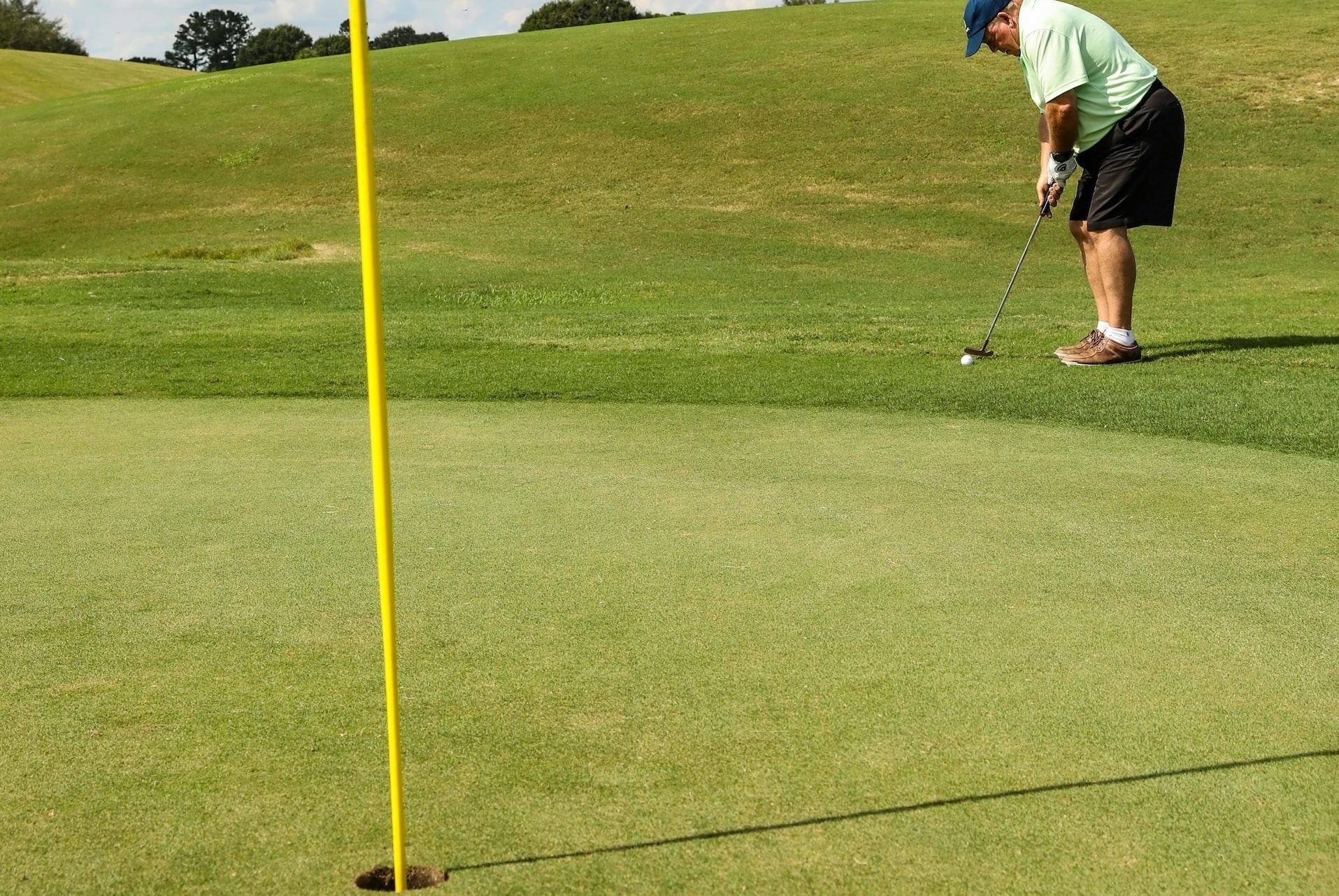 A senior golfer at a hole with flag putting from just off the green with 
