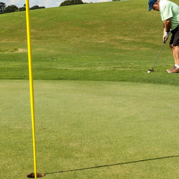 A senior golfer at a hole with flag putting from just off the green with 