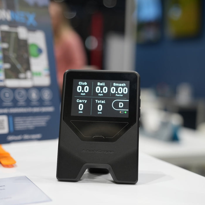 The Shot Scope LM1 golf launch monitor with lit-up display standing on a white display desk at the 2026 PGA Show