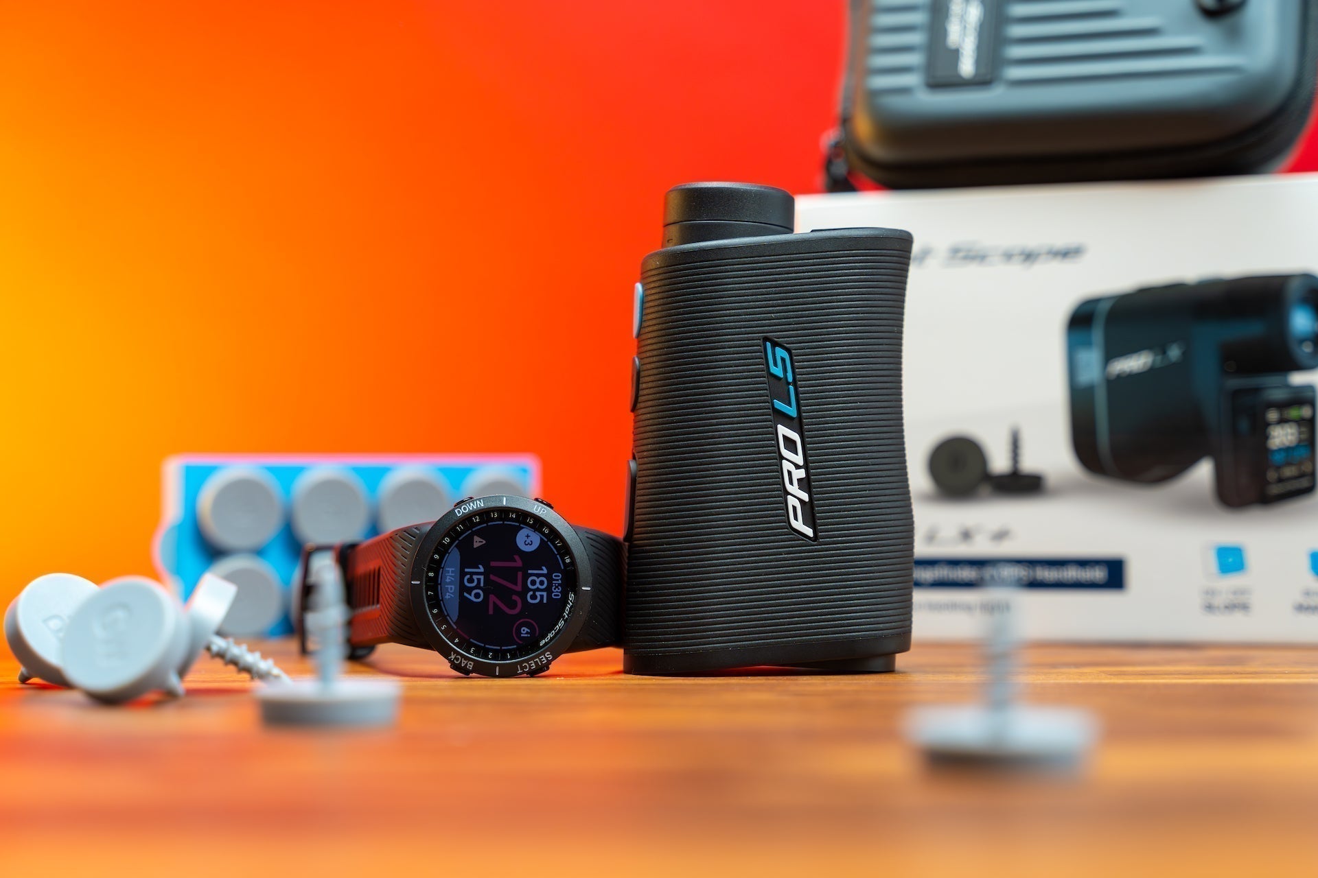Shot Scope golf tech products on a woodgrain surface with a bright orange background
