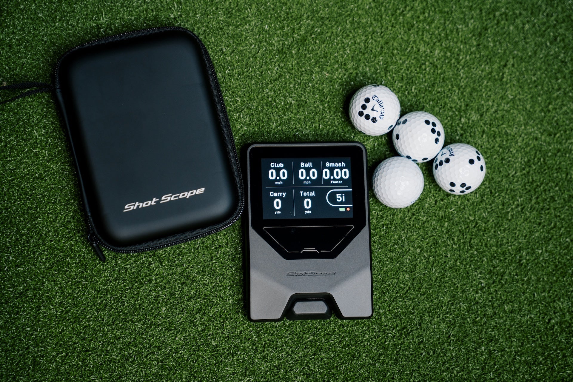 Shot Scope LM1 laying on a golf mat with its carrying case and golf balls