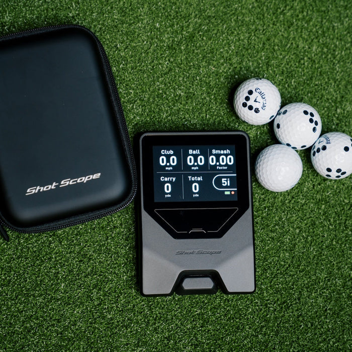 Shot Scope LM1 laying on a golf mat with its carrying case and golf balls