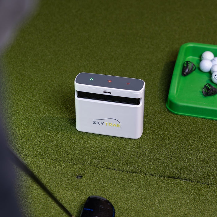 A SkyTrak+ golf launch monitor on a golf hitting mat next to a tray of golf balls