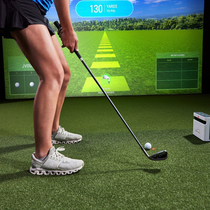 The lower half of a female golfer getting ready to hit a golf ball with an iron in front of a SkyTrak+ launch monitor in a home golf simulator