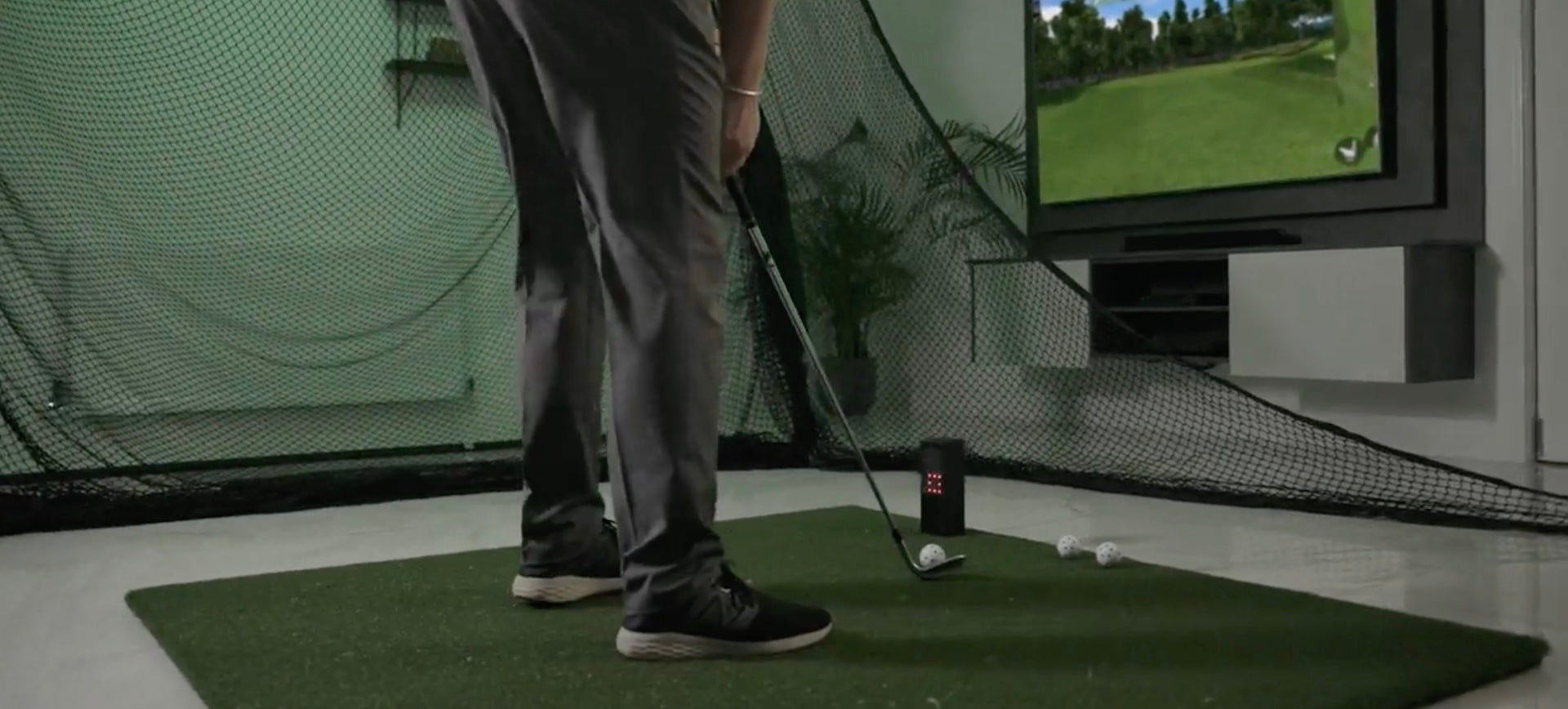 A golfer getting ready to hit with a Square Golf launch monitor in an indoor simulator with a golf hitting net, golf practice mat, and flatscreen TV