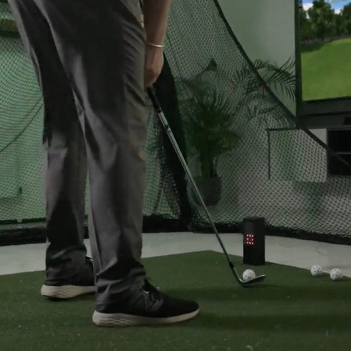 A golfer getting ready to hit with a Square Golf launch monitor in an indoor simulator with a golf hitting net, golf practice mat, and flatscreen TV
